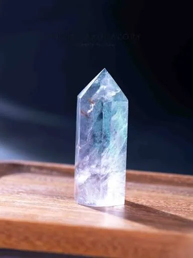 A polished translucent crystal point with blue, violet and pale green bands in a beam of light
