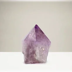 A small polished purple crystal point on a light neutral surface